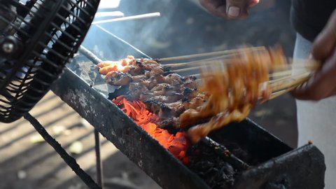 Chicken satay on traditional charcoal fire. satay on fire with smoke and an appetizing look. hands cooking satay on the grill
