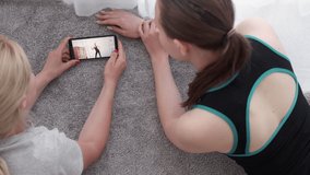 Dance fitness. Female trainer. Video lesson. Home sport. Unrecognizable two women watching fit lady showing tutorial steps on mobile phone in light room interior.