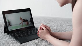 Fitness trainer. Online sport. Home gym. Video lesson. Unrecognizable woman watching laptop with fit lady showing correct plank workout in light room interior.
