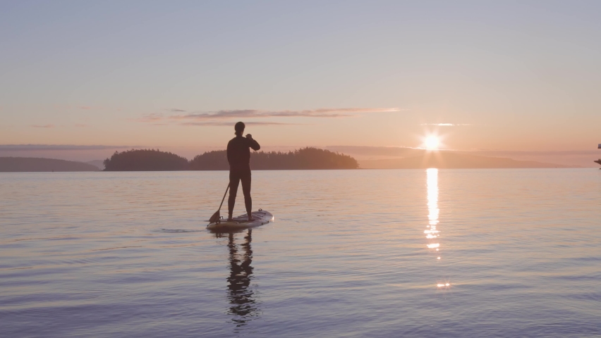 Adventurous Caucasian Adult Woman on a Stand Up Paddle Board is paddling on the West Coast of Pacific Ocean. Sunny Sunrise. Victoria, Vancouver Island, BC, Canada. Slow Motion Royalty-Free Stock Footage #1079744087
