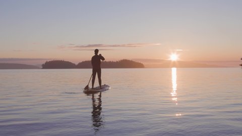 Adventurous Caucasian Adult Woman on a Stand Up Paddle Board is paddling on the West Coast of Pacific Ocean. Sunny Sunrise. Victoria, Vancouver Island, BC, Canada. Slow Motion