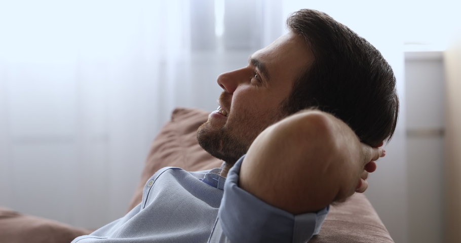 Close up side view mindful young male homeowner relaxing on comfortable couch, daydreaming or napping in living room, breathing fresh air, enjoying peaceful weekend relaxation moment alone indoors. Royalty-Free Stock Footage #1079755490