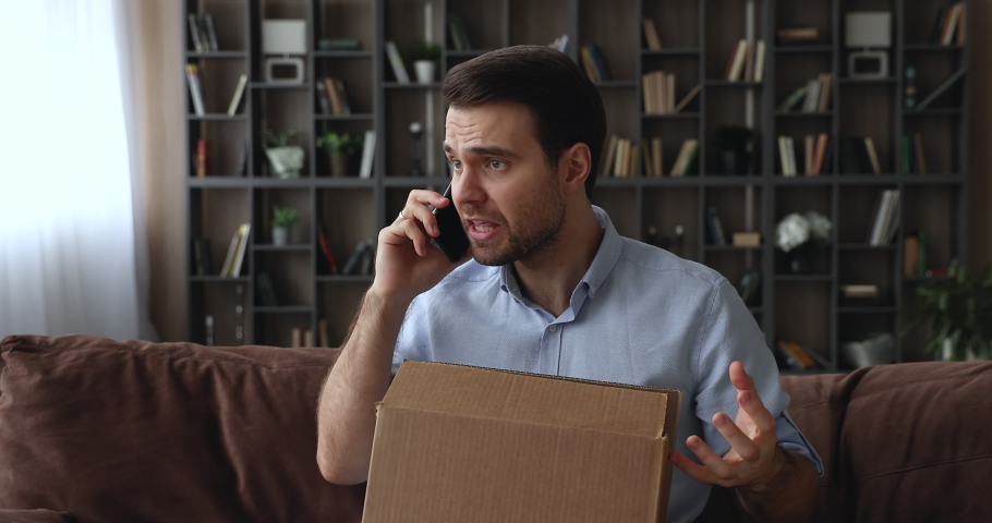 Angry unhappy young man holding phone call conversation with seller or delivery company manager, dissatisfied with wrong order or crashed item when opened carton parcel, negative shopping experience.