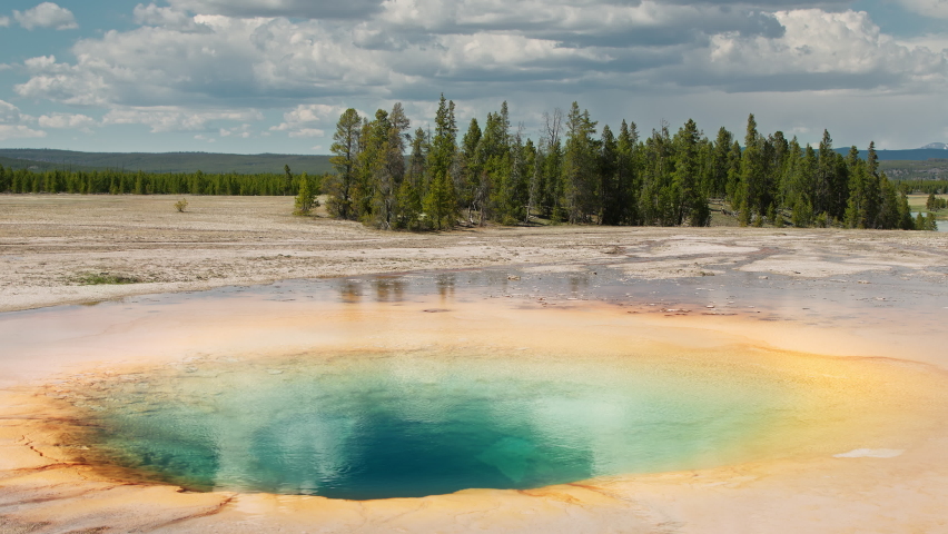 Yellowstone National Park view vibrant colorful Hot Spring geyser basin 4K footage. Cinematic Yellowstone landscape with transparent water blue green sulfur hole with green pine forest on background
