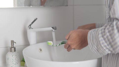 Close-up, a woman brushes her teeth in the morning with a brush with toothpaste in the bathroom by the sink.
