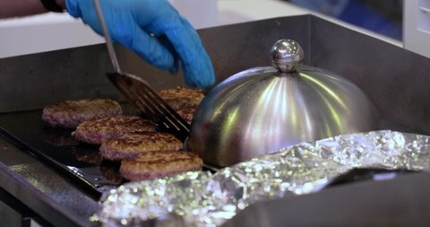 Meat beef patty is cooked in a hot frying pan. Street food, chef flips burgers with a spatula.
