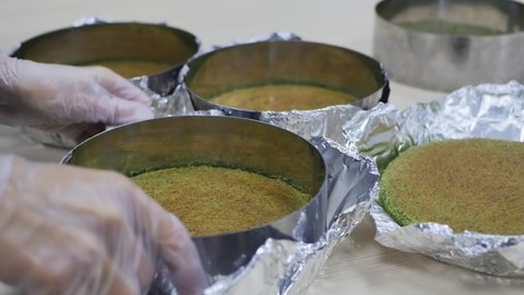 the hands of a pastry chef woman in pink gloves remove baked green spinach cakes from molds and foil to make a sponge cake. Slow motion, close-up
