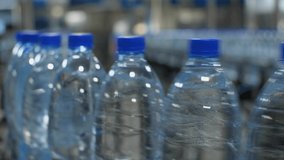 Blurry video of a blue plastic water bottle moving along a conveyor belt. Production of mineral water at a food processing plant