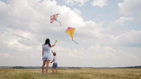 Happy family, mom and son, playing with flying kite on meadow in beautiful sunny day, blue sky. Happy young mother and kid boy launch kite on nature.