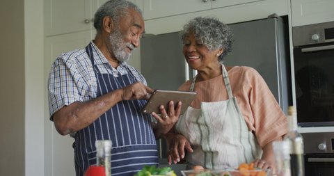  happy african american senior couple cooking together, using tablet. healthy, active retirement lifestyle at home.