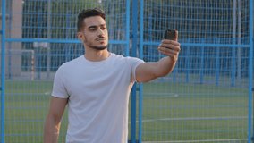 Young sports blogger Indian guy in sportswear looking at smartphone camera records broadcasts from stadium, communicates with audience. Middle Eastern athlete uses cellphone for video conferencing