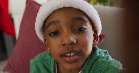 Happy african american boy wearing santa hat having video call at christmas time. 
