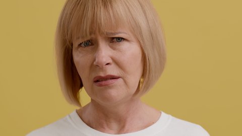 Closeup Portrait Of Disgusted Senior Woman Looking At Camera And Frowning Face, Displeased Middle Aged Female Feeling Aversion While Standing Over Yellow Studio Background, Slow Motion Footage