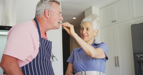 Happy caucasian senior couple wearing aprons cooking together in kitchen. 