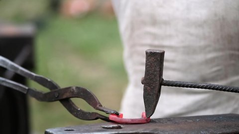 Close-up of forging a horseshoe. The blacksmith teaches the apprentice to knock on a red-hot horseshoe with a hammer. Training in blacksmithing.
