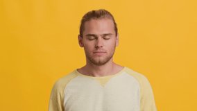 Portrait Of Tired Young Guy Yawning, Exhausted Millennial Man Covering Mouth With Hand, Feeling Bored And Sleepy While Standing Isolated Over Yellow Studio Background, Slow Motion Footage