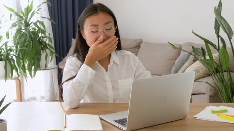 Exhausted asian attractive business woman yawn working with her notebook sitting at her desk