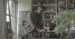 Mid adult hispanic male using laptop in kitchen