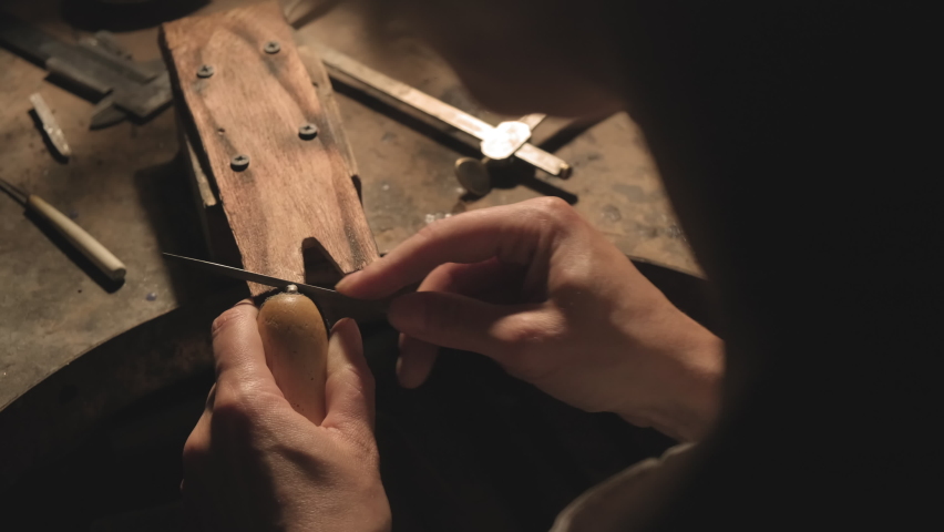 A jeweler polishes a product with a file in a dark workshop. A jeweler makes a product in his workshop by performing various processes. Close-up. Macro. The jeweler installs the piece in the clip