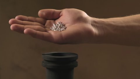 Hand staged throws silver pieces into a crucible for melting metal. Hand staging throws silver into a crucible for melting metal