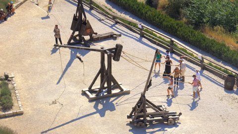 Les Baux-de-Provence, France - August 2021 : Tourists practicing catapult shooting with an actor during an animation and guided tour
