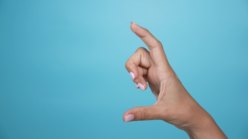 Close-up view 4k stock video footage of 1 female hand forming gesture as if showing big and small sizes of virtual invisible object with help of two fingers isolated on bright blue color background Royalty-Free Stock Footage #1079798699