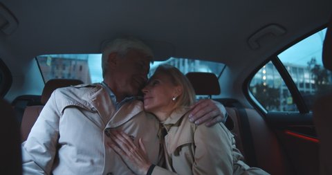 Happy mature couple embracing in backseat of car. Portrait of romantic senior man and woman hugging and cuddling in taxi