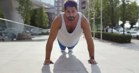 Indian man doing workout exercise outdoors in city. Portrait of male doing push-up exercise on sidewalk in city. Active lifestyle concept