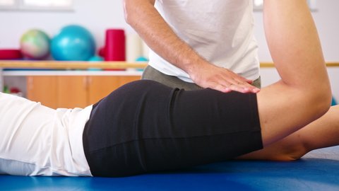 Close-up shot of a Caucasian male physiotherapist giving exercise therapy for sciatica to a female patient in a supine position.