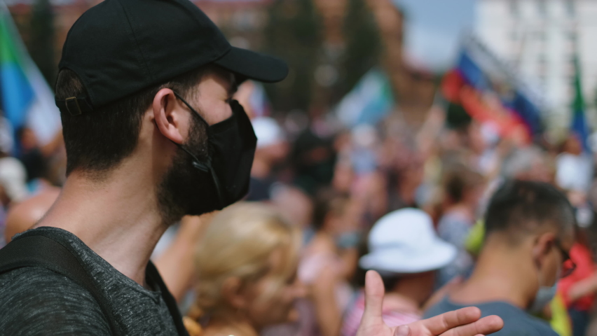 Political rally activist protester in black cap and coronavirus facemask applauds. Rebel in crowd in covid-19 face mask applauds. Strike demonstration guy. Opposition resistance protest revolt riot Royalty-Free Stock Footage #1079803844