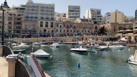 Panoramic footage of a harbour with yachts in Malta. Boats in marina in front of cityscape.