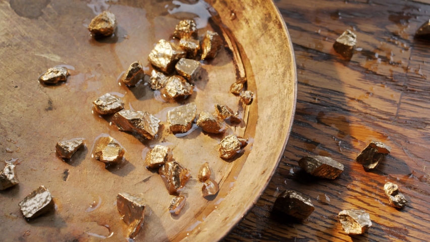 Male hands are fingering several pieces of gold nuggets over a bowl for washing the gold sand.  Royalty-Free Stock Footage #1079805689