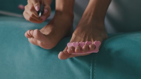 Unrecognizable barefoot female softening toenails cuticle with oil on feet while sitting on couch at home