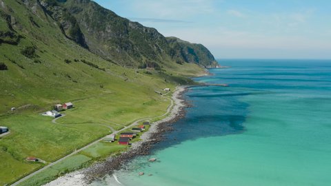Aerial decent footage revealing green flourishing mountain by the sea, farm houses by the shoreline, turquoise ocean waves meeting a white silver sandy beach Refvik Måløy Norge