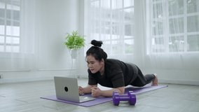 Fat woman exercises by following video clips on her laptop to lose weight in her living room at home.
