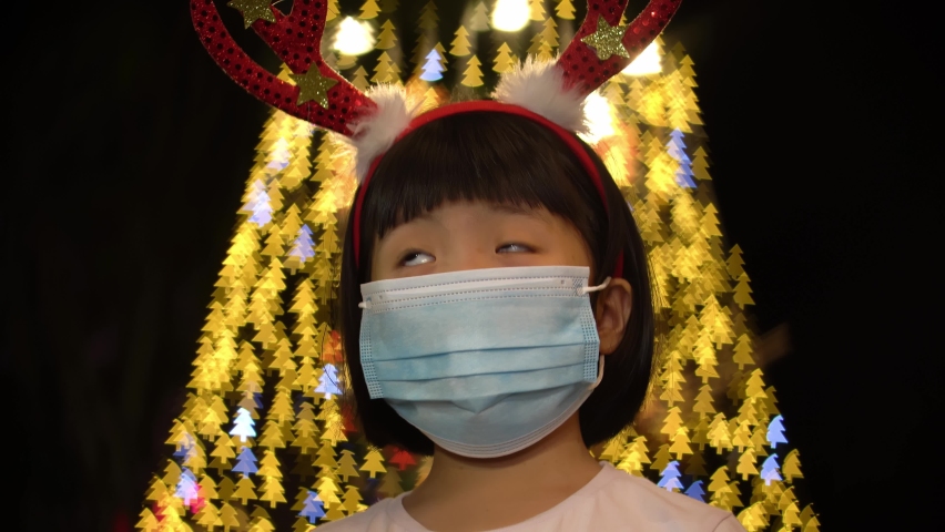 Selective focus little girl with face mask with Christmas tree bokeh light background