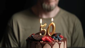 Fifty year old man blows out burning numbers 50 candles on chocolate cake and claps your hands. Birthday cake for 50 years anniversary. Slow Motion. - Powered by Shutterstock - Get 15% off with code: PIKWIZARD15