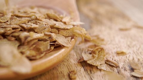 Dry wheat spelt flakes. Falling uncooked breakfast cereal on a rustic wooden spoon in slow motion. Macro. Healthy food concept