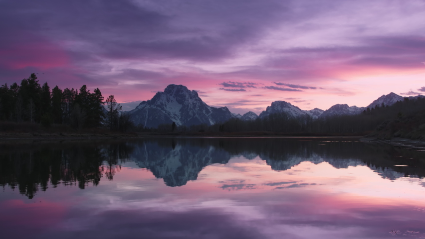 Summer sunset sky. Panoramic landscape sunset in Nature park. 4K Grand Teton National park, USA. Pink skyline sunset mountains. Wilderness travel colorful sky. Vibrant sunset reflecting in lake waters