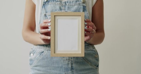 A view of a person holding a beige frame with white blank space on a white wall