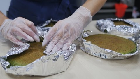the hands of a woman pastry chef in pink gloves are wrapping fresh baked biscuits in foil with green spinach. Slow motion. Cooking spinach cake