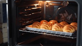 Video clip person hand in oven glove holding aluminium tray contained baked croissants with nonstick baking sheets foil. Croissants making process, fresh from the oven theme. (selective focus)
