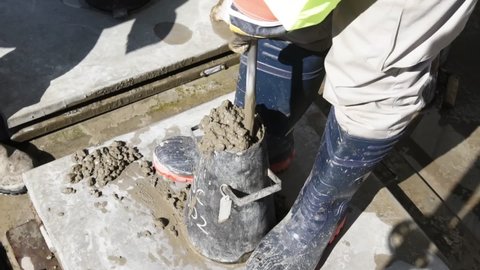 Man In Boots Tamping Concrete In A Slump Cone With Steel Tamping Rod. high angle