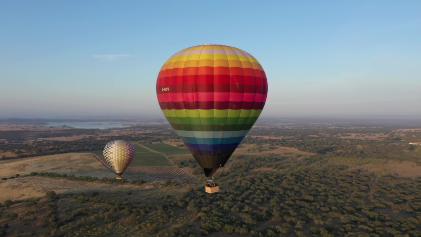Colorful hot air balloons flying above the rural plains of Alentejo in Portugal at sunrise with beautiful sky background - wide view from high altitude aerial drone - Adventure travel concept
 Royalty-Free Stock Footage #1079836442