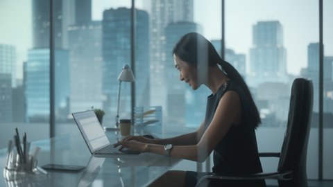 Excited Businesswoman in Stylish Dress Sitting at a Desk in Modern Office, Using Laptop Computer. Successful Manager Ecstatic About Winning a Real Estate Investment Deal for Corporate Business.