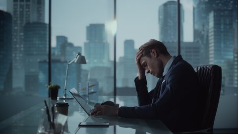 Stressed Out Businessman in a Suit Sitting at a Desk in Modern Office, Using Laptop Computer. Tired and Busy Manager Working on Financial and Marketing Projects for Corporate Business.
