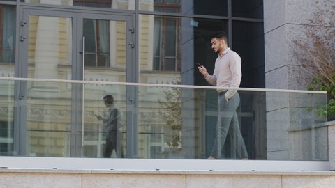 Successful business man boss leader worker manager well-dressed guy walks on balcony terrace in company office looking at mobile phone chatting online with smartphone reads good news makes video call