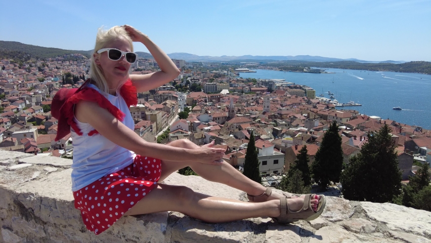 Elegant woman sitting on the walls of the St. Michael castle. Aerial view over the port of Sibenik. Sibenik historic city of Croatia in Dalmatia. Fortress with best view of the Cathedral of St. James.