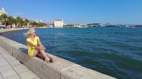 Woman sitting and sunbathing on the waterfront of Split city and famous ferry boat port. Spit city of Croatia in Dalmatia in summer. Ancient Roman Empire town and Roman Emperor, Diocletian's Palace.