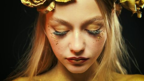Portrait divine fantasy woman goddess. Girl skin is covered with gold colored shimer. Cheekbones of face covered with shiny sparkle glitters. Theatrical makeup, black eyelash extensions golden shadows